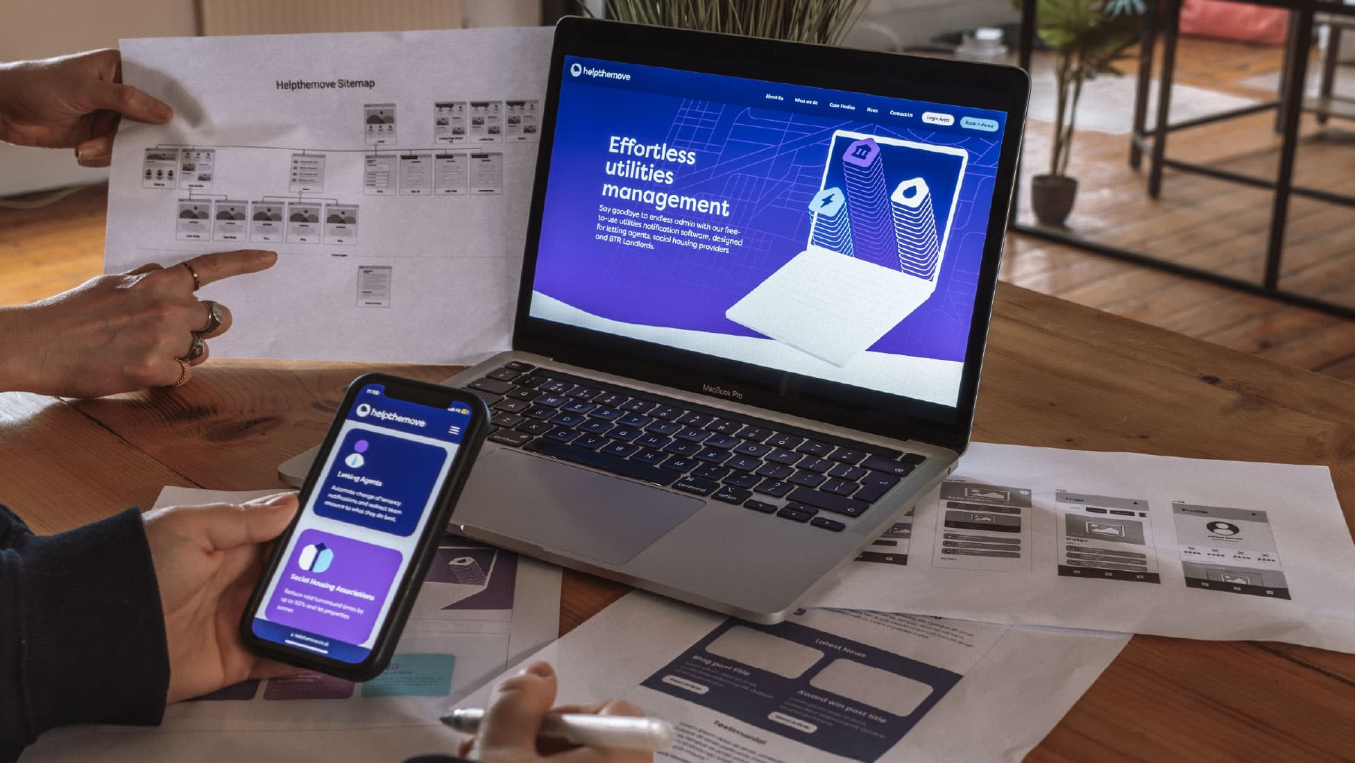 Laptop and phone showing website design. Wireframe and sitemap sheets scattered on table