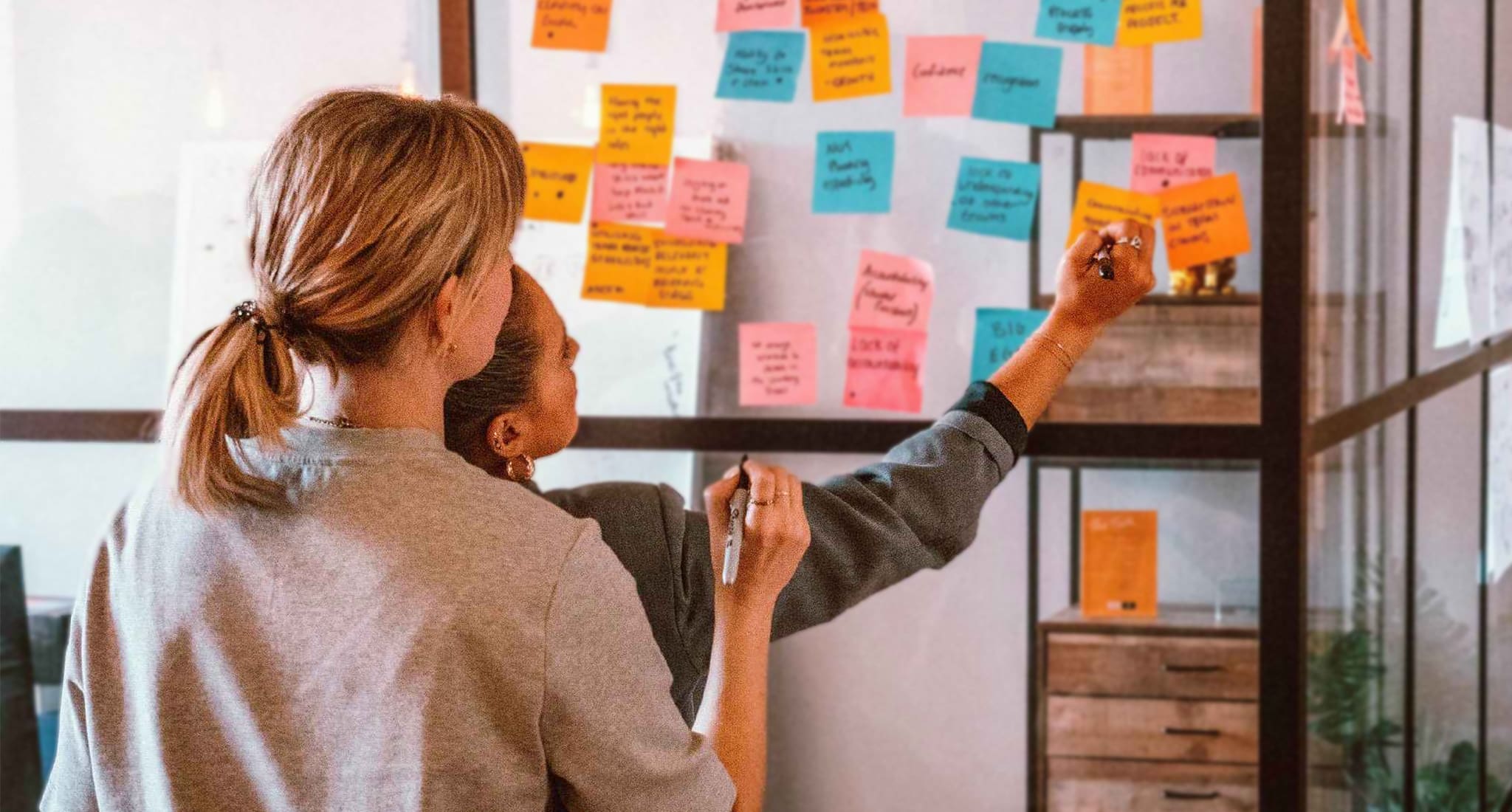 Team members drawing on post it notes on glass wall