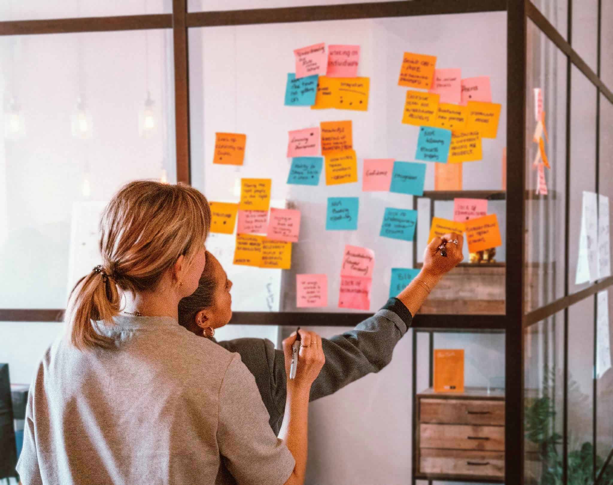 Team members drawing on post it notes on glass wall